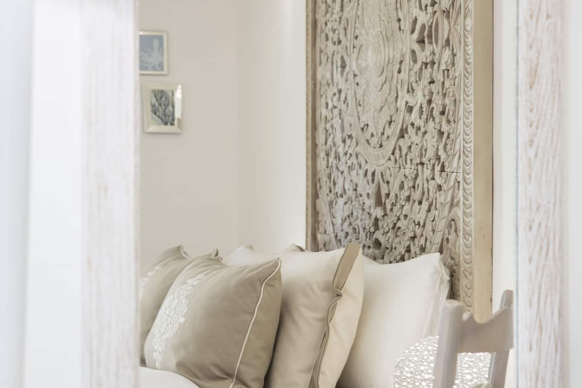 A room with a white bed, beige pillows, a decorative wall panel, and a hanging light fixture.