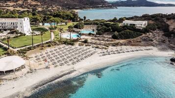Vista aerea di un resort costiero con spiaggia, piscina e un edificio grande con numerosi balconi.