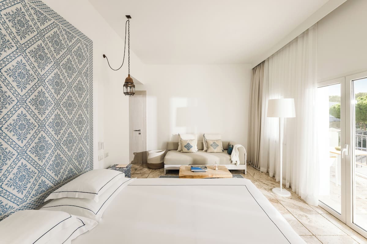 A hotel room with a bed, a sofa, a coffee table, a lamp, and a view of the outdoors.