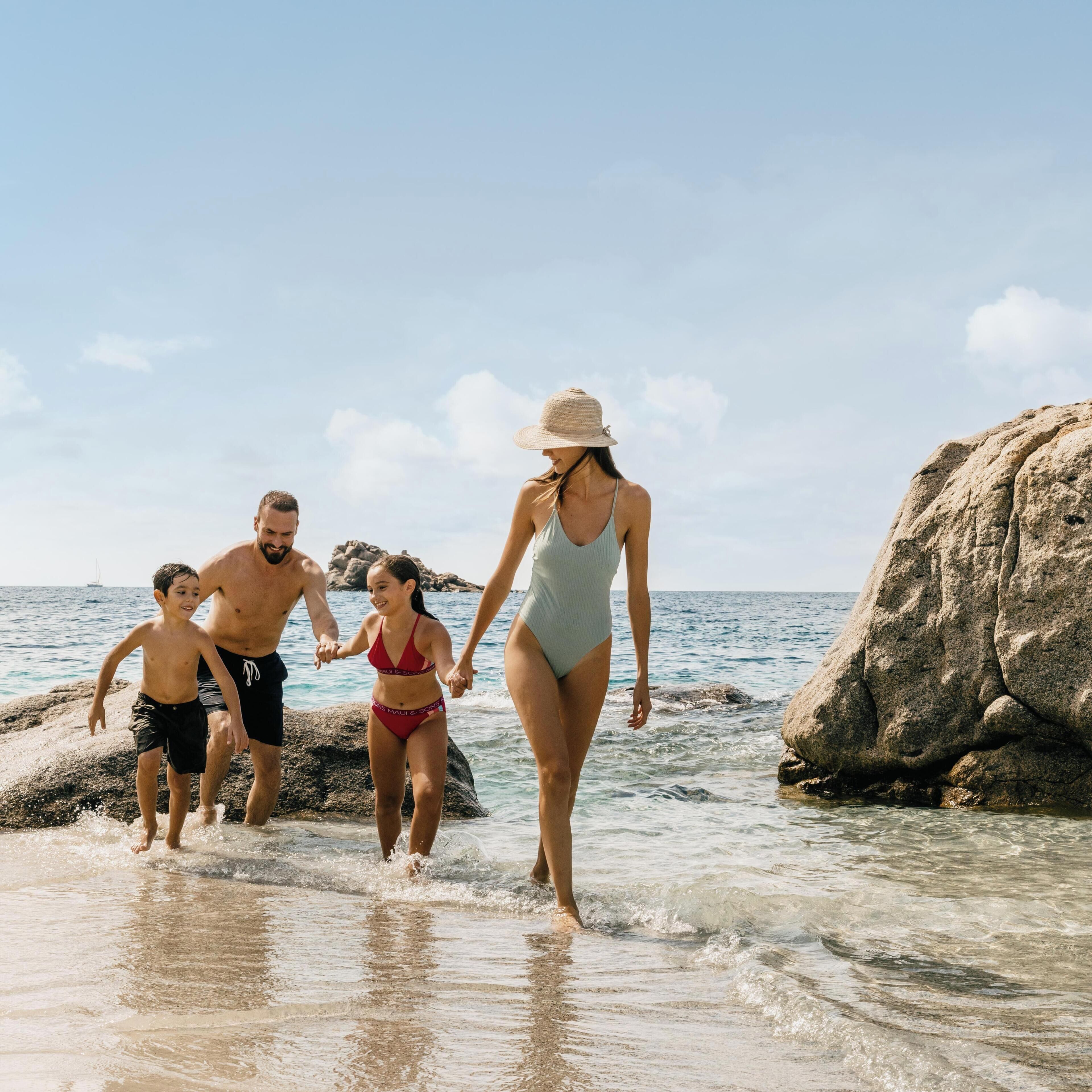 Una familia caminando sobre una playa rocosa con agua cristalina y una gran formación de rocas.