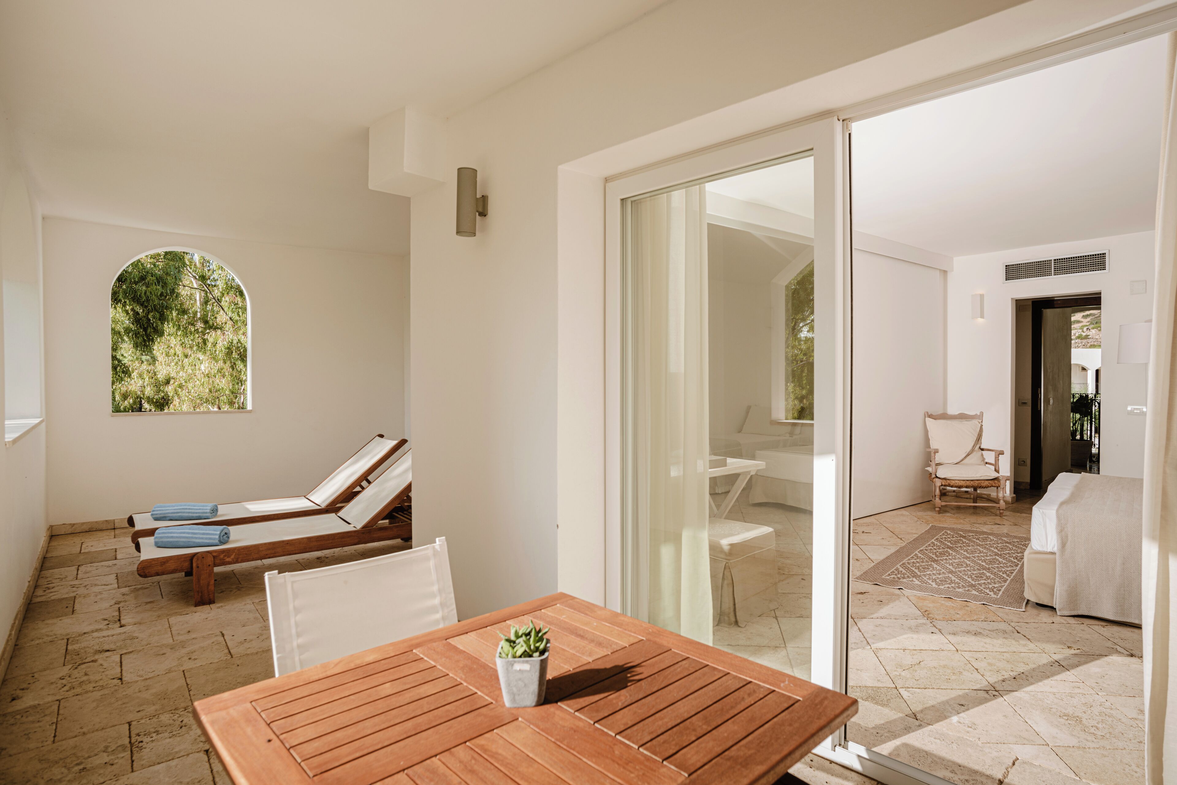 A room with a wooden table, a potted plant, and a view of a garden through a window.