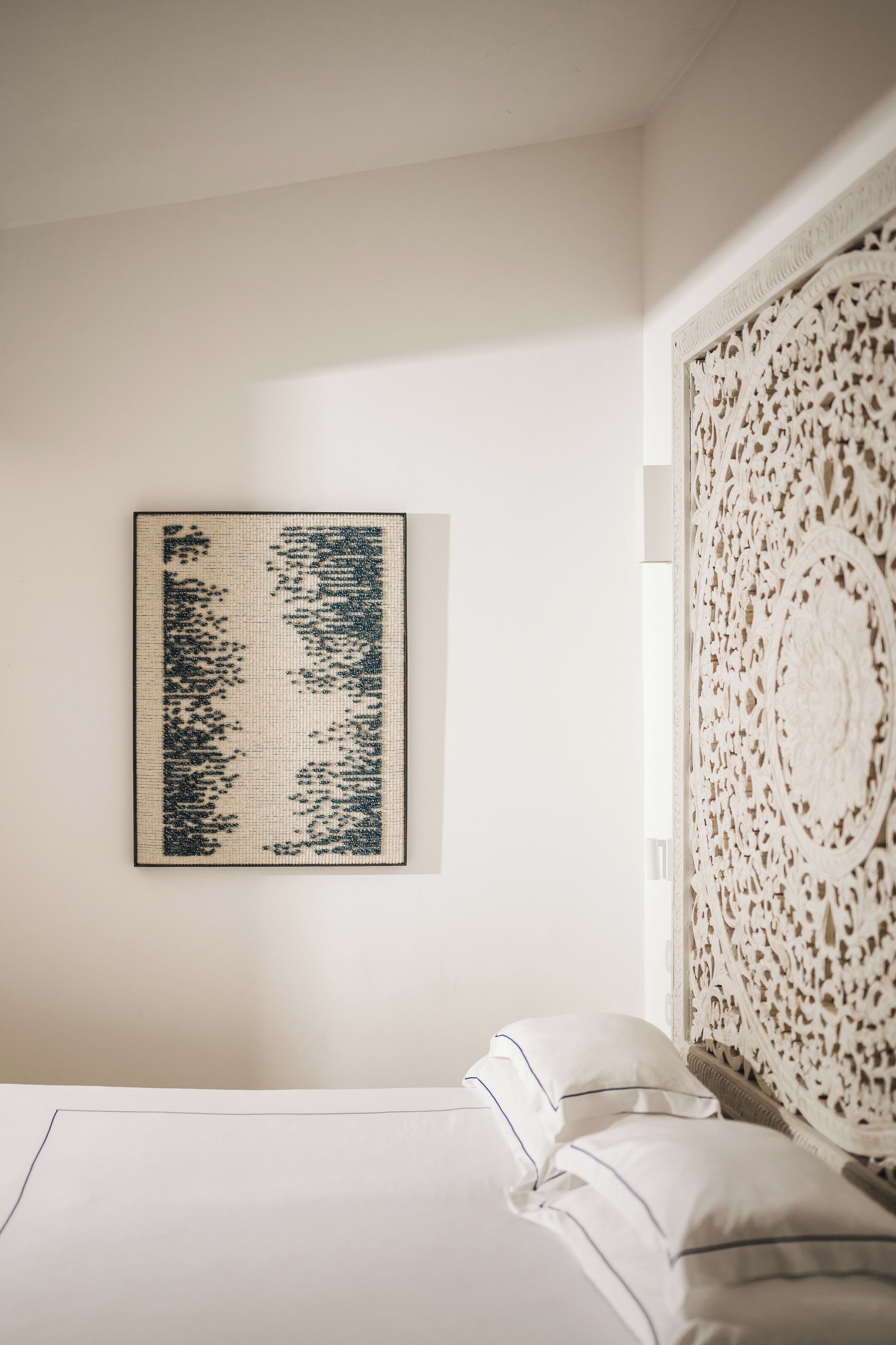 A minimalist bedroom with a bed, a wall-mounted artwork, and a decorative headboard.