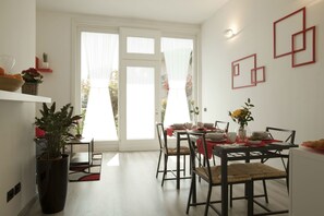 Uma zona de refeições moderna com uma mesa posta para quatro pessoas, rodeada por cadeiras, e um vaso de planta em primeiro plano.