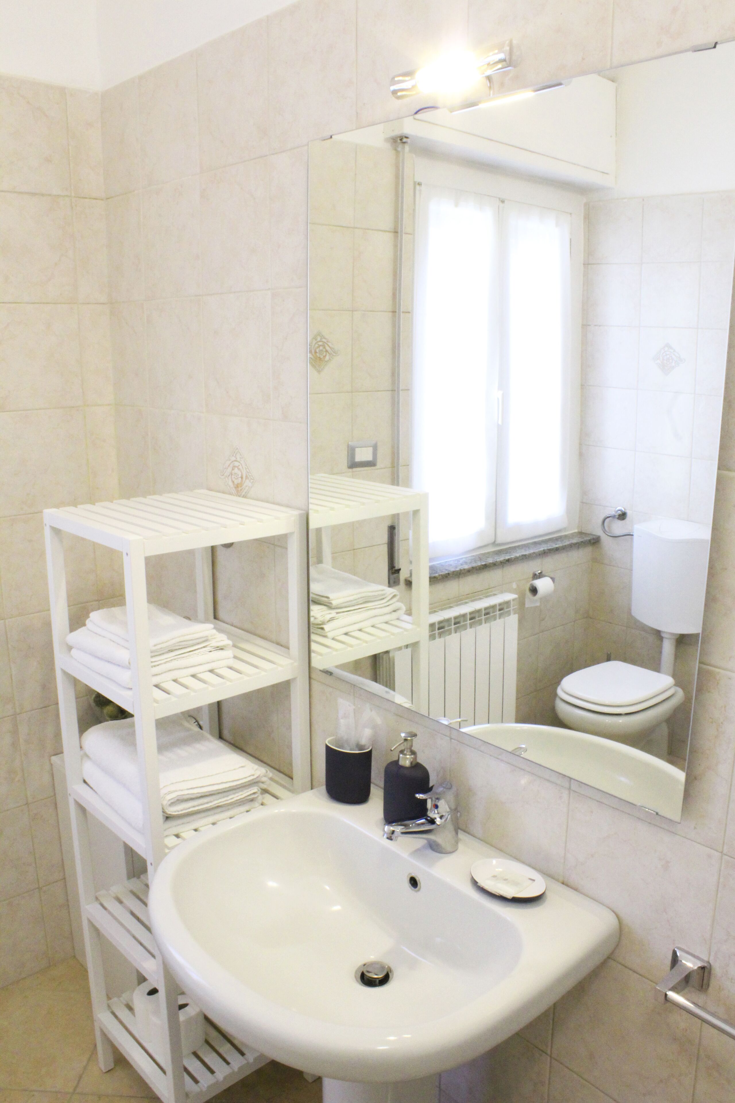 Un baño con lavamanos blanco, un espejo, inodoro y una ventana con cortinas.