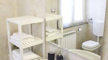 Un baño con lavamanos blanco, un espejo, inodoro y una ventana con cortinas.
