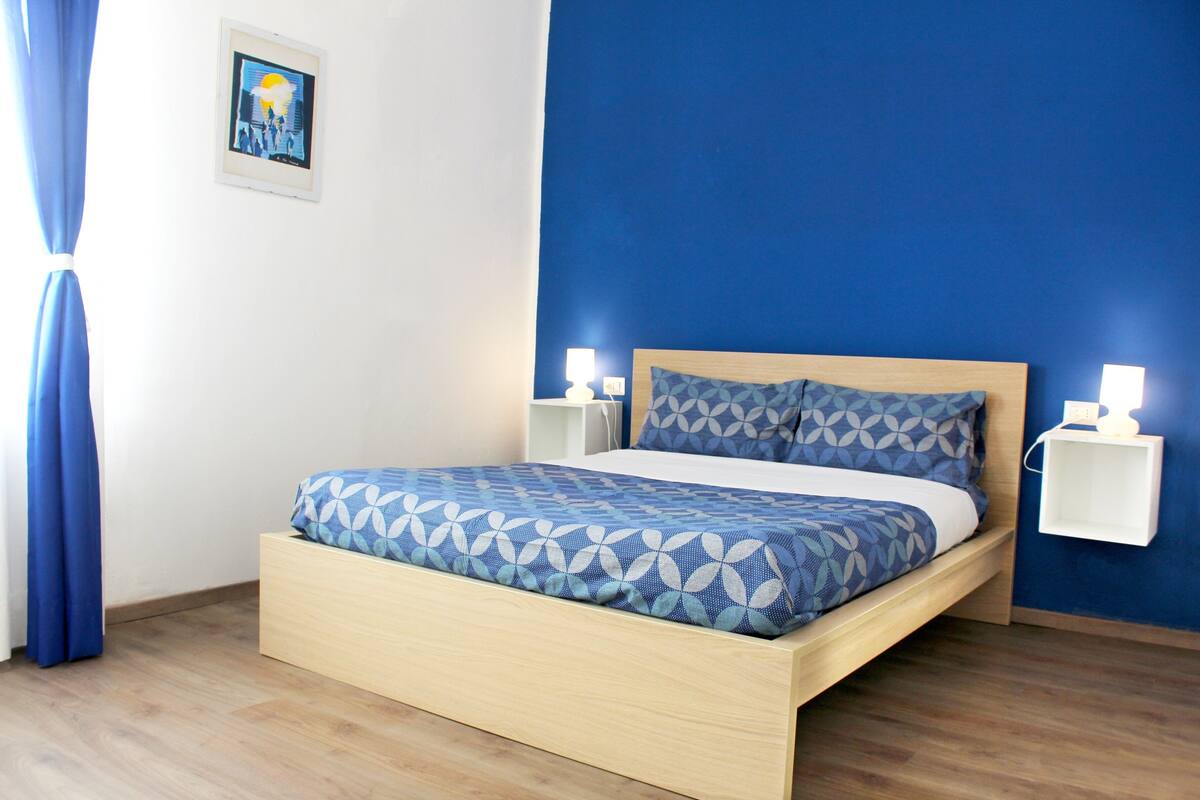 A bed with a geometric patterned bedspread, wooden headboard, and two bedside lamps.