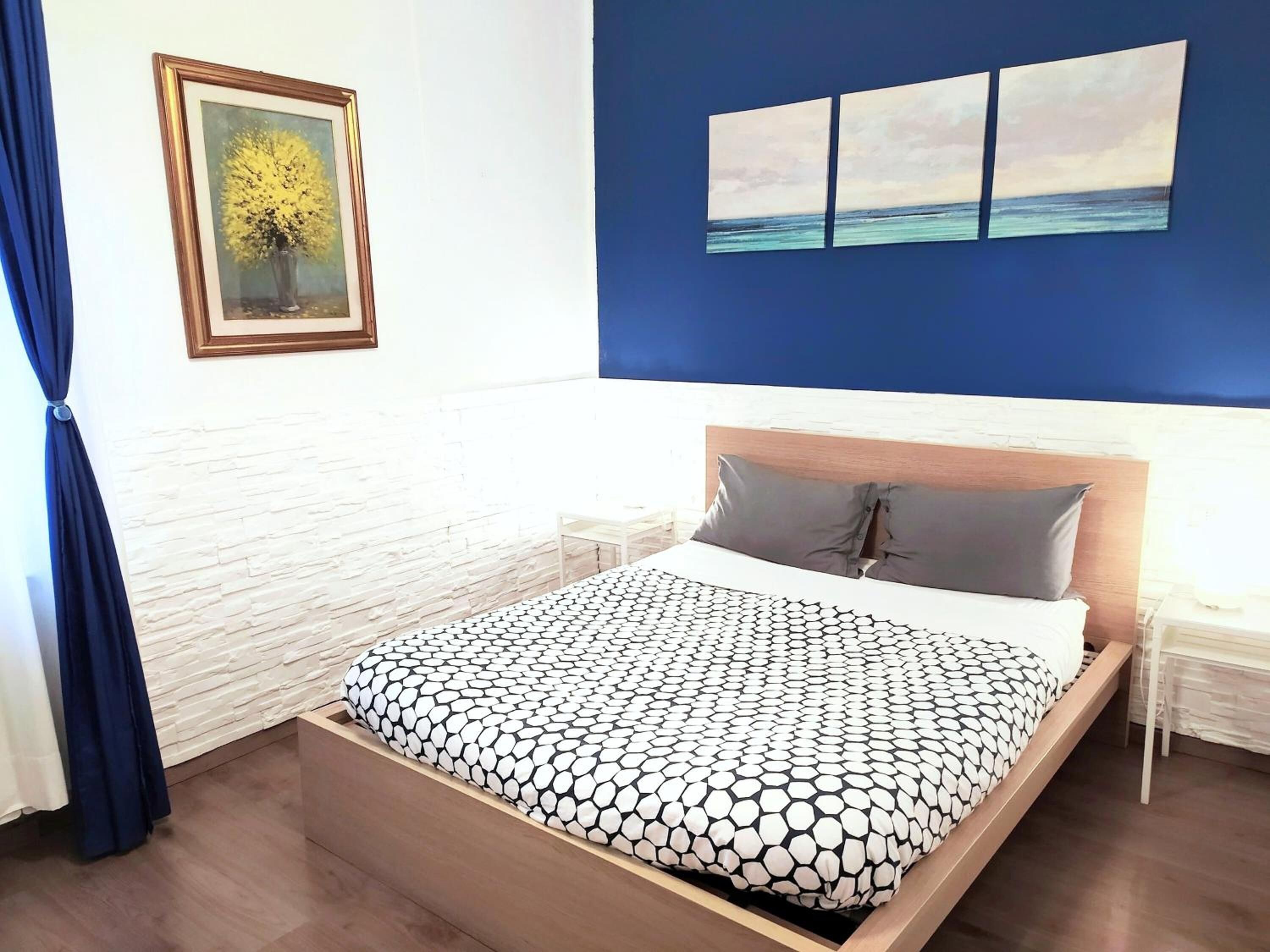 Un dormitorio con cama, mesita de noche, un cuadro enmarco y una pared con tres cuadros.