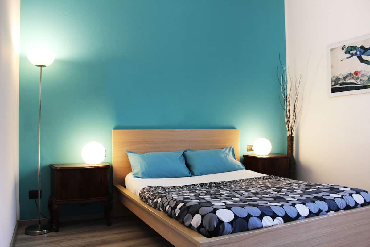 A neatly made bed with a patterned bedspread, two matching pillows, and two bedside lamps.