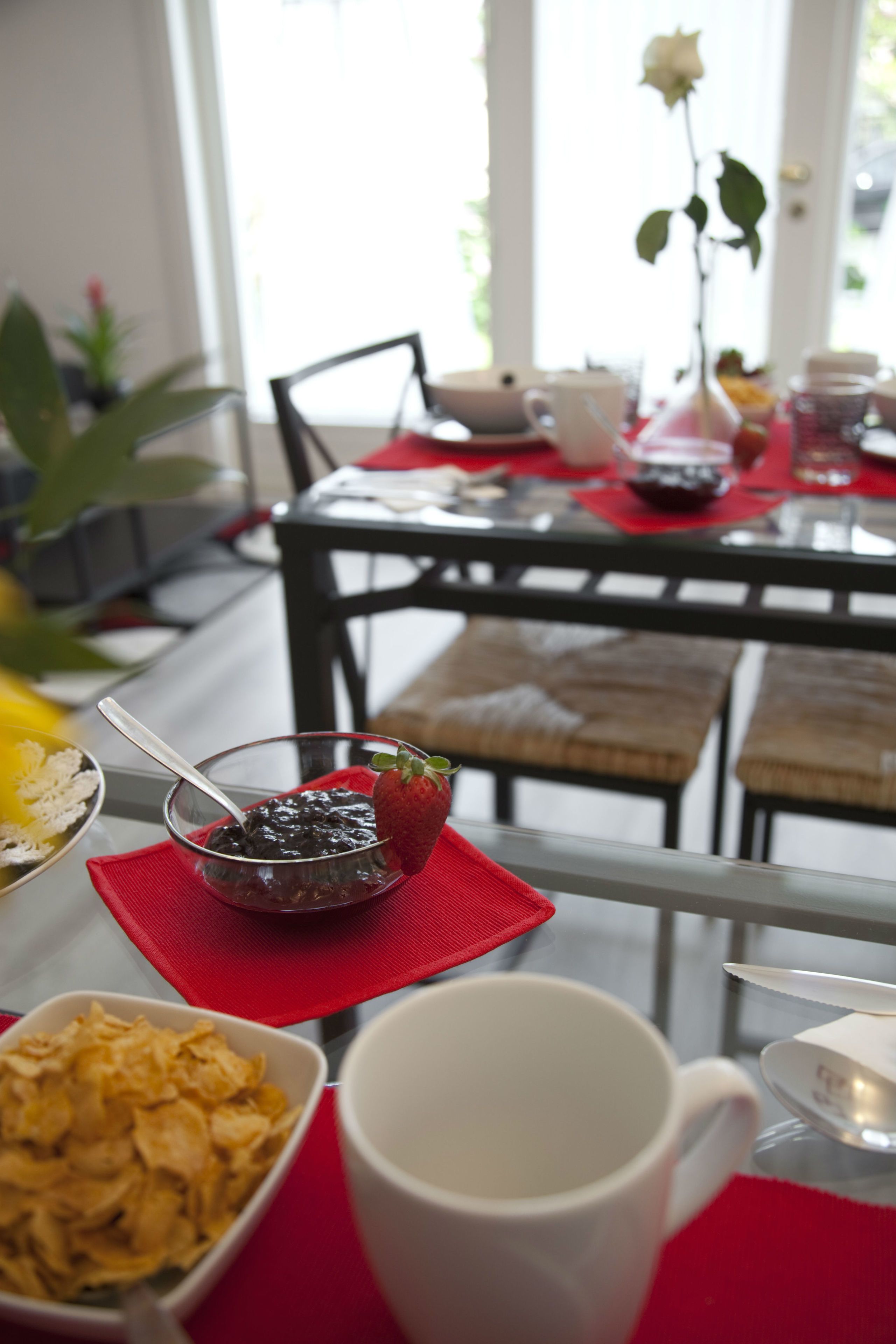 A dining table with a bowl of cereal, a mug, and a small dish with a strawberry.