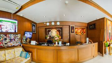 A reception area with a wooden reception desk, a sofa with floral upholstery, a wall-mounted television, and a bulletin board with photos.
