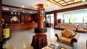 A spacious lobby with a reception desk, comfortable seating, a decorative pillar, and a large window offering a view of the outdoors. - Mammoth Resort (Khon Kaen)