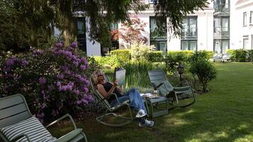 Eine Person entspannt in einem Stuhl in einem gepflegten Garten mit Blick auf ein Gebäude im Hintergrund.