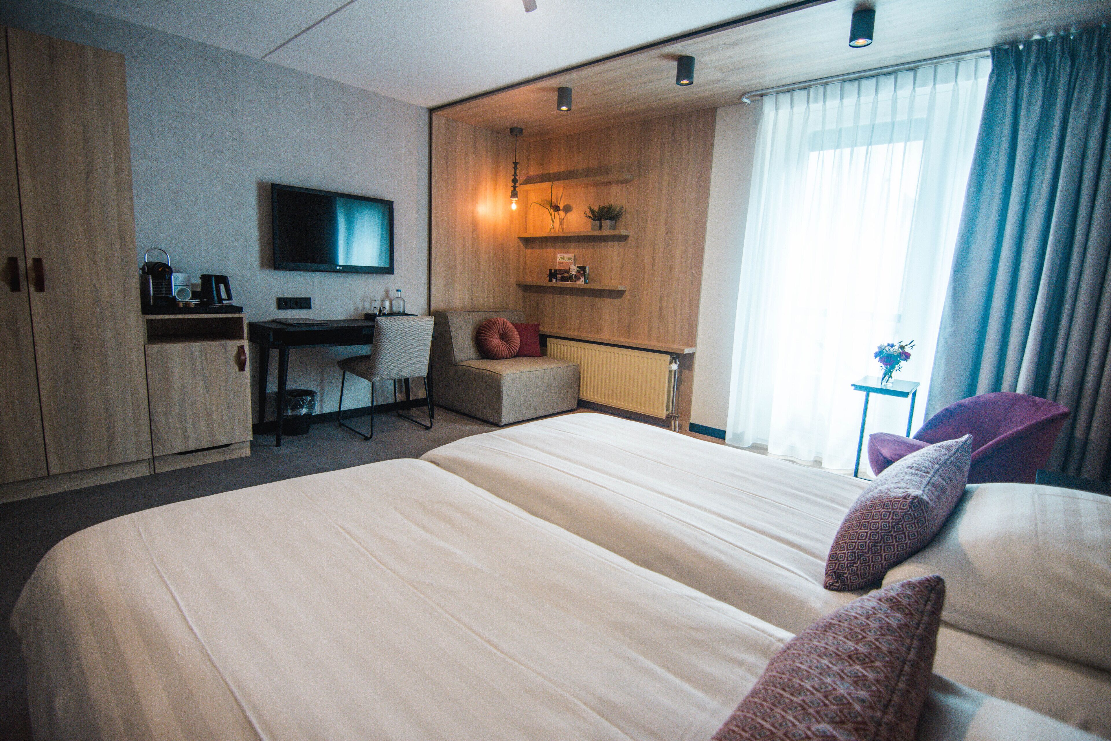 Una habitación de hotel moderna con una cama grande, un escritorio, una silla, un televisor y una ventana con cortinas.
