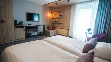 Una habitación de hotel moderna con una cama grande, un escritorio, una silla, un televisor y una ventana con cortinas.