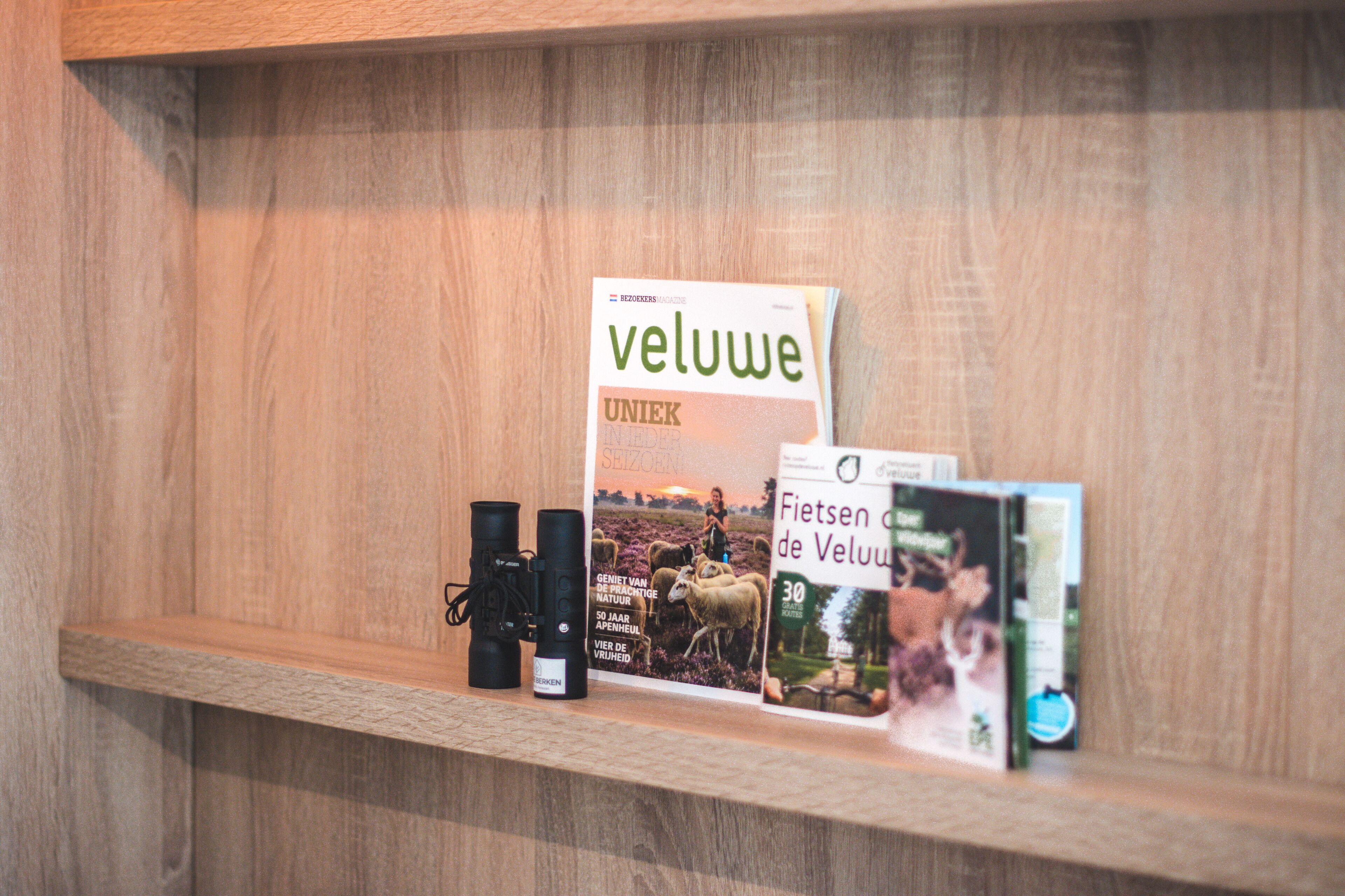 Una estantería de madera con un libro titulado 'veluwe' y un par de prismáticos.
