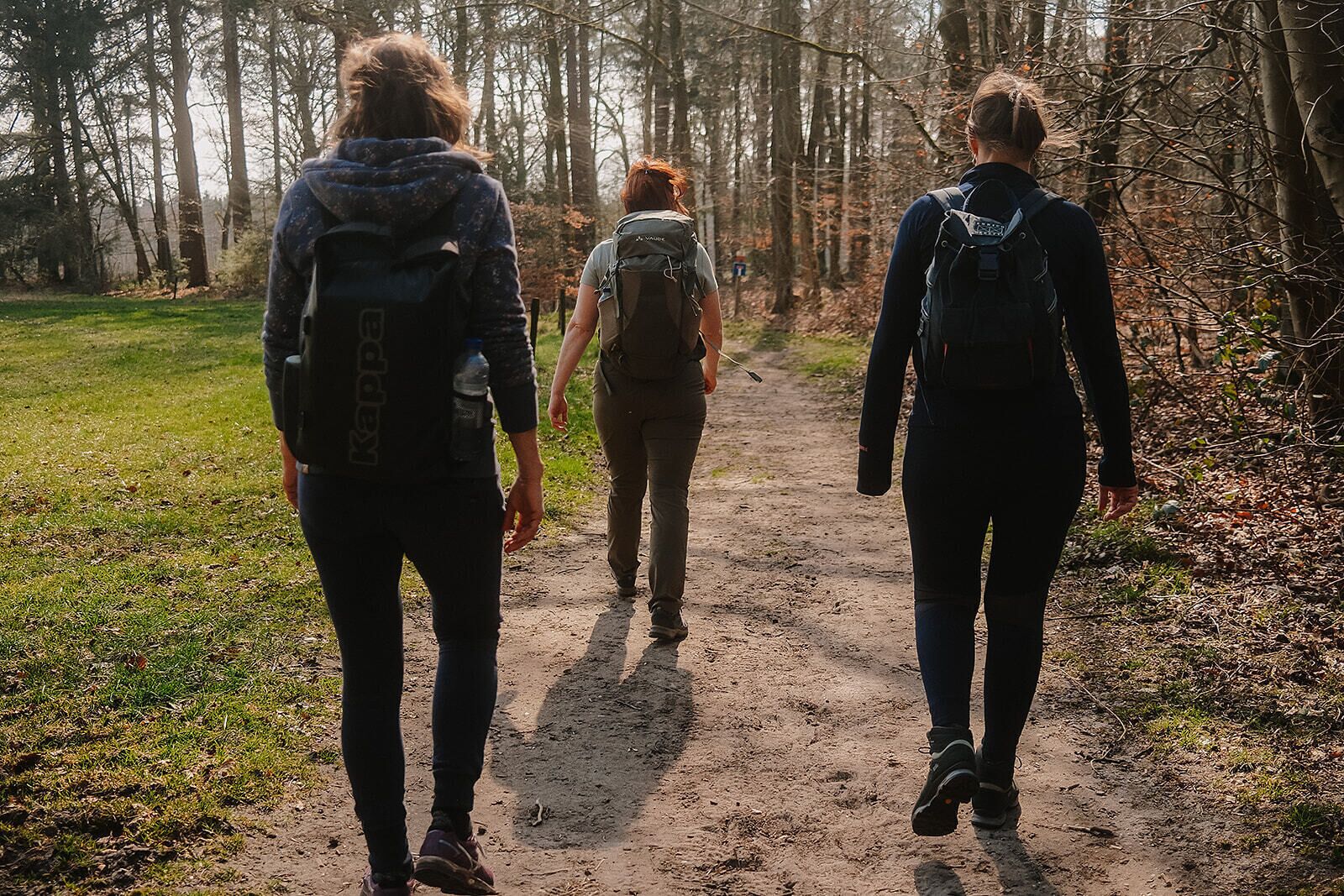 Tre persone camminano su un sentiero sterrato in una zona boschiva.