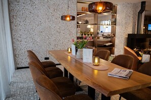 A dining area with a wooden table, brown upholstered chairs, a menu, and a vase with flowers. - Witte Berken Natuurhotel (Epe)