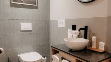 Een moderne badkamer met een grote ovale spiegel, een schilderij van een paard in een lijst, een witte wasbak en een houten wastafelmeubel met opbergruimte.
