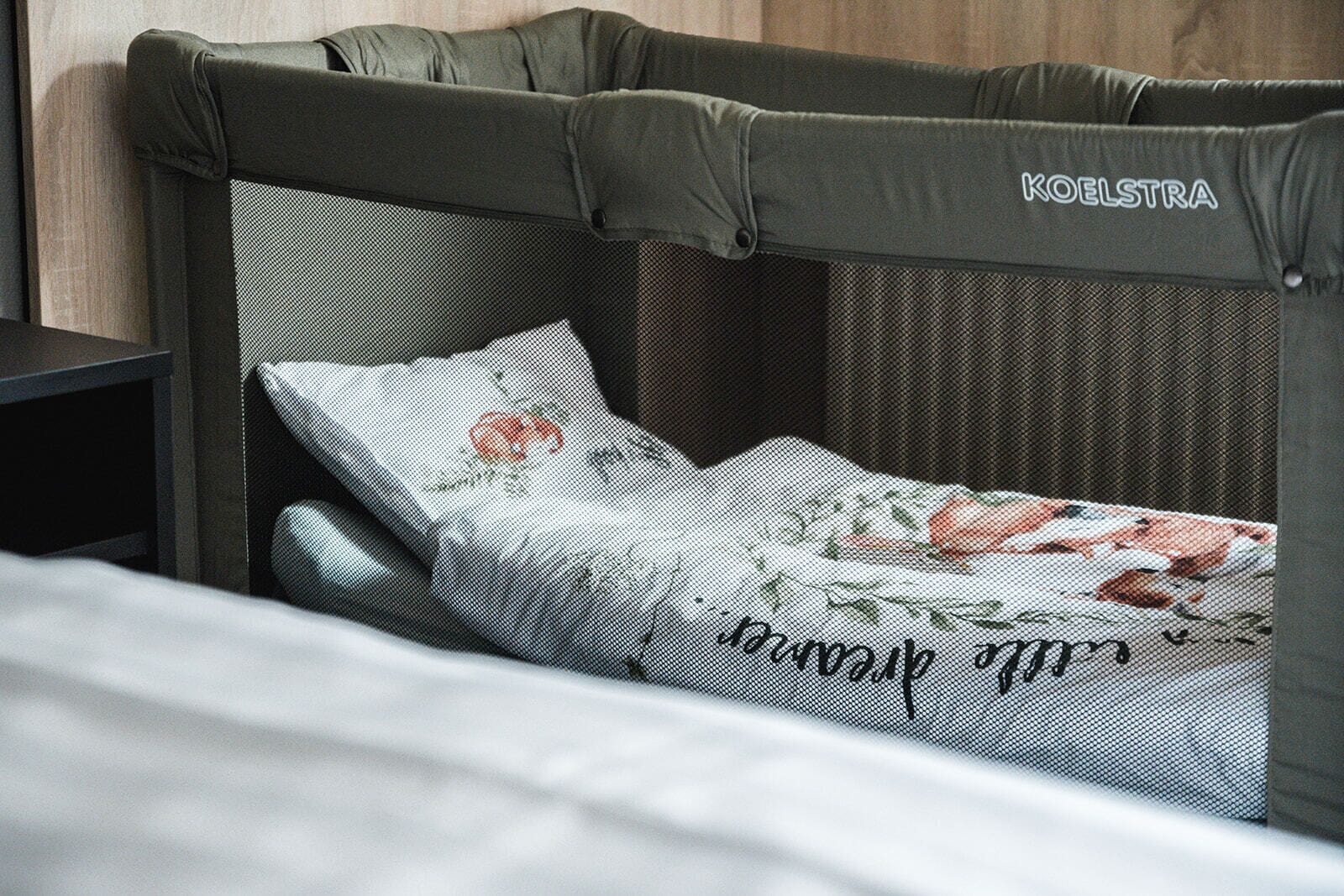 Een bed met hoofdbord met de tekst 'KOELSTRA', een sierlijk gebloemd kussen en een wit laken.
