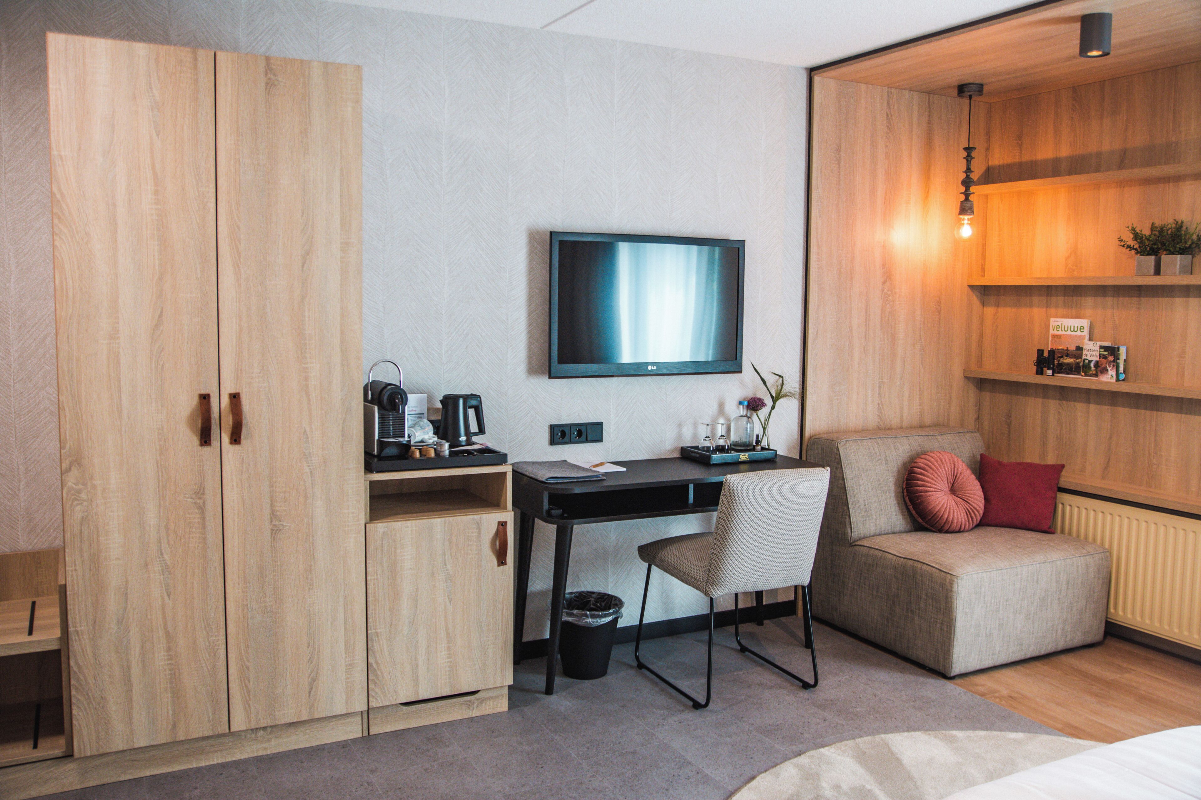 Una habitación moderna con un armario de madera, un escritorio con silla, televisor, sofá y un radiador.