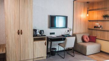 Una habitación moderna con un armario de madera, un escritorio con silla, televisor, sofá y un radiador.