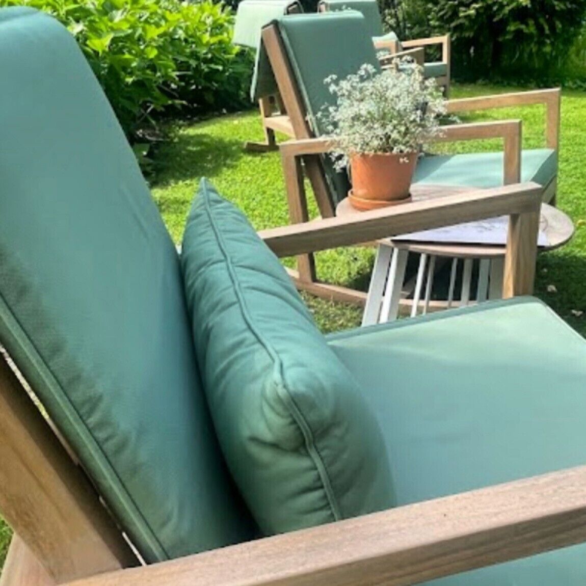A green outdoor seating area with a wooden table and chairs, surrounded by greenery.