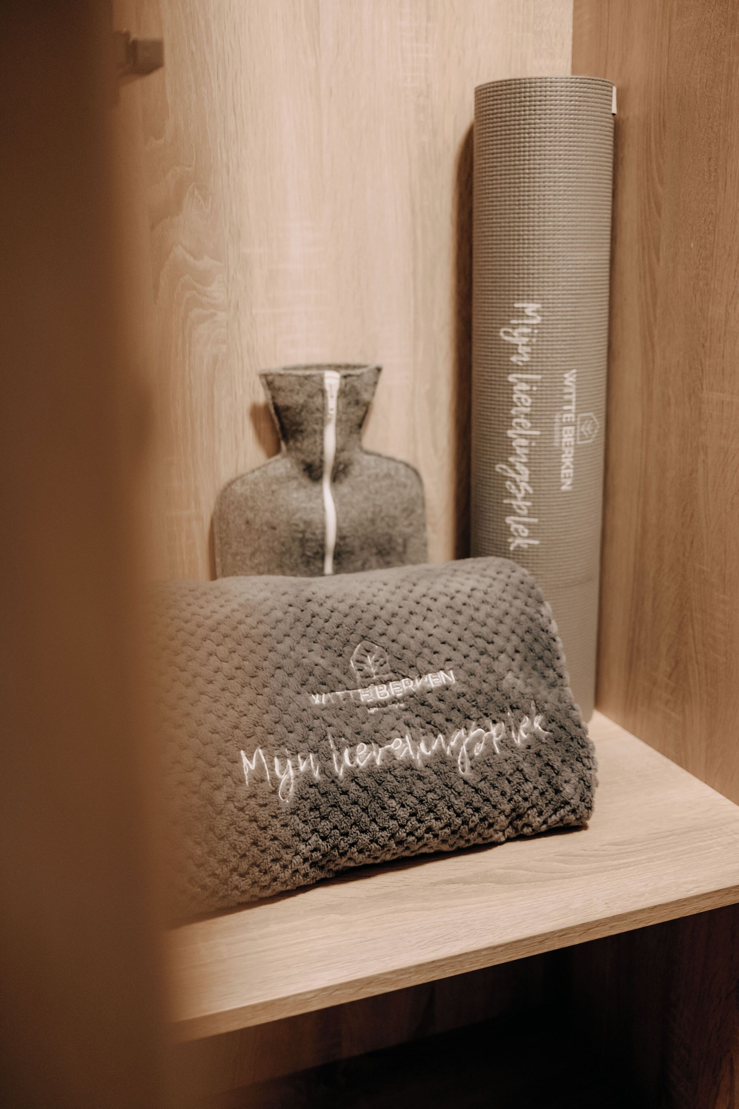 A neatly arranged yoga mat, a small decorative vase, and a rolled-up yoga mat on a wooden shelf.