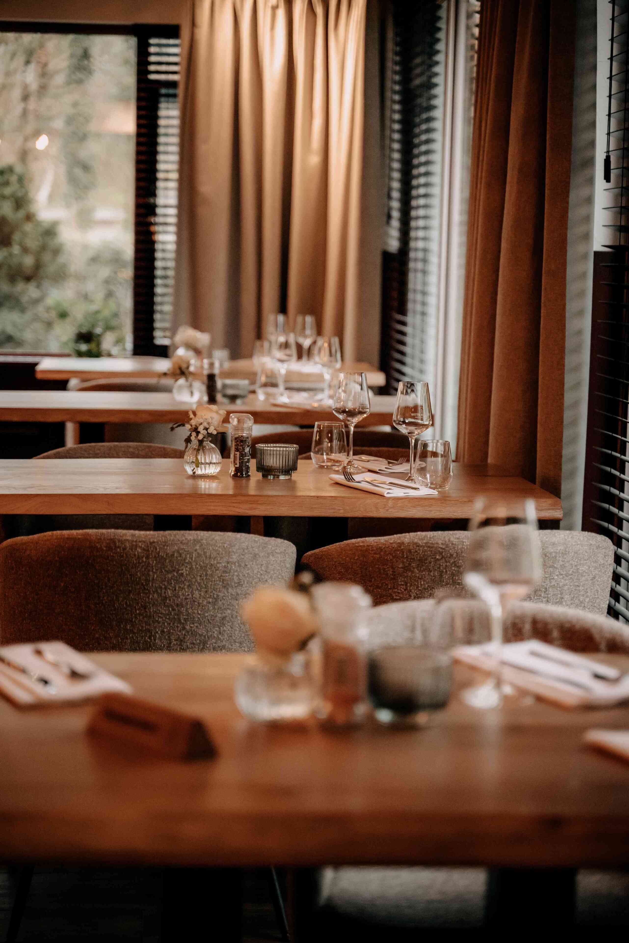 Restaurante con mesas de madera dispuestas para comer, con cristalería y pequeños objetos decorativos.