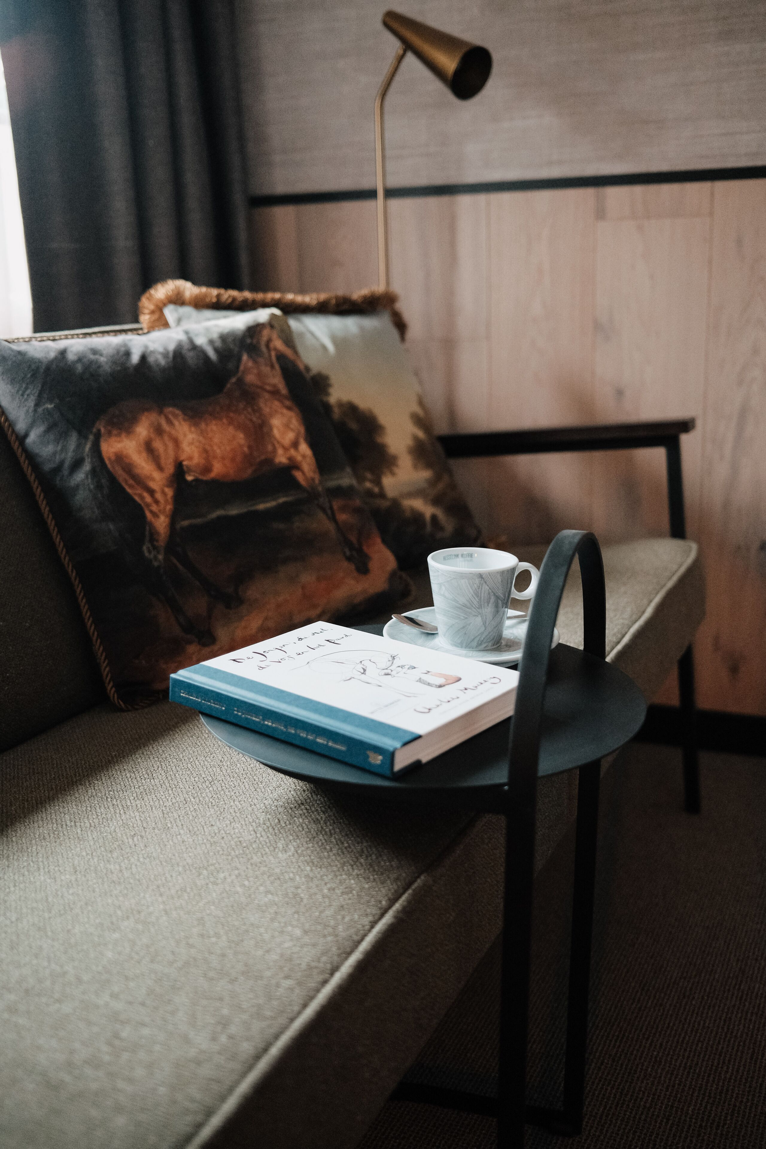 A room with a sofa, a side table, a book, a cup, and a lamp.