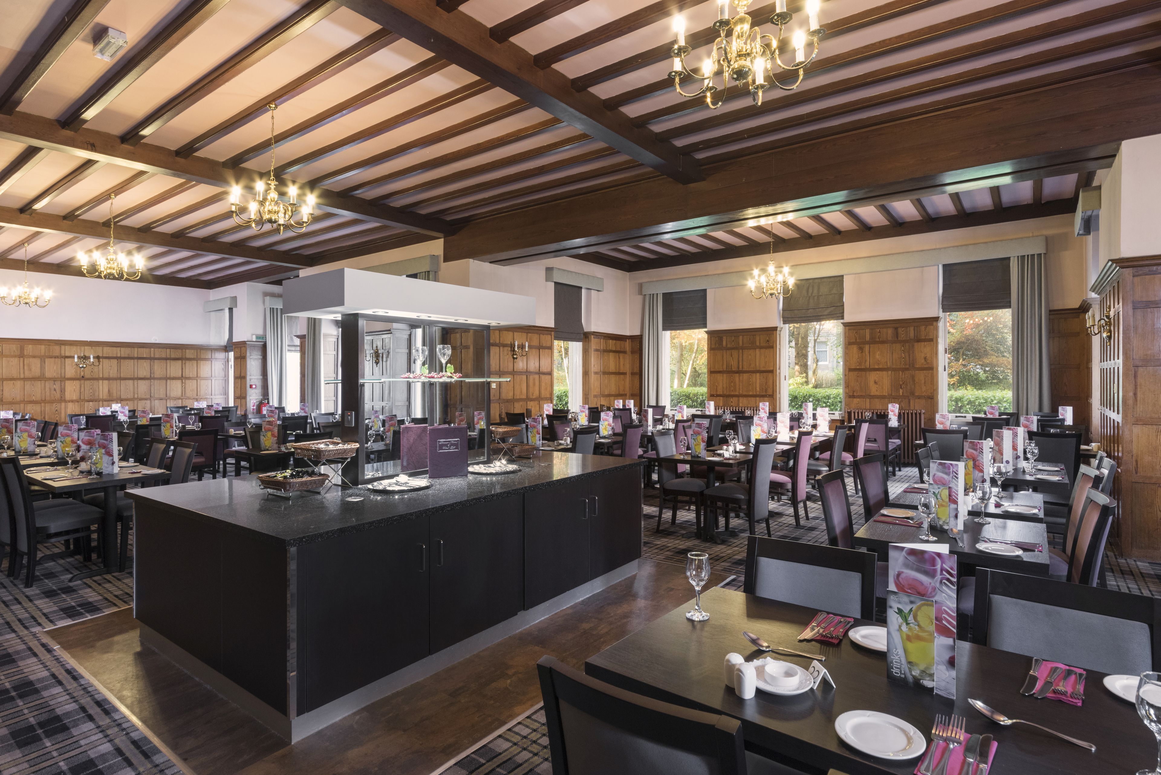 A spacious dining area with a central island, wooden beams on the ceiling, and large windows providing natural light.