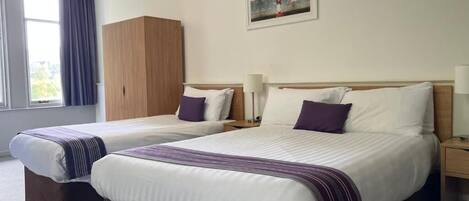 A hotel room with two beds, a wardrobe, a painting on the wall, and a window with curtains.
