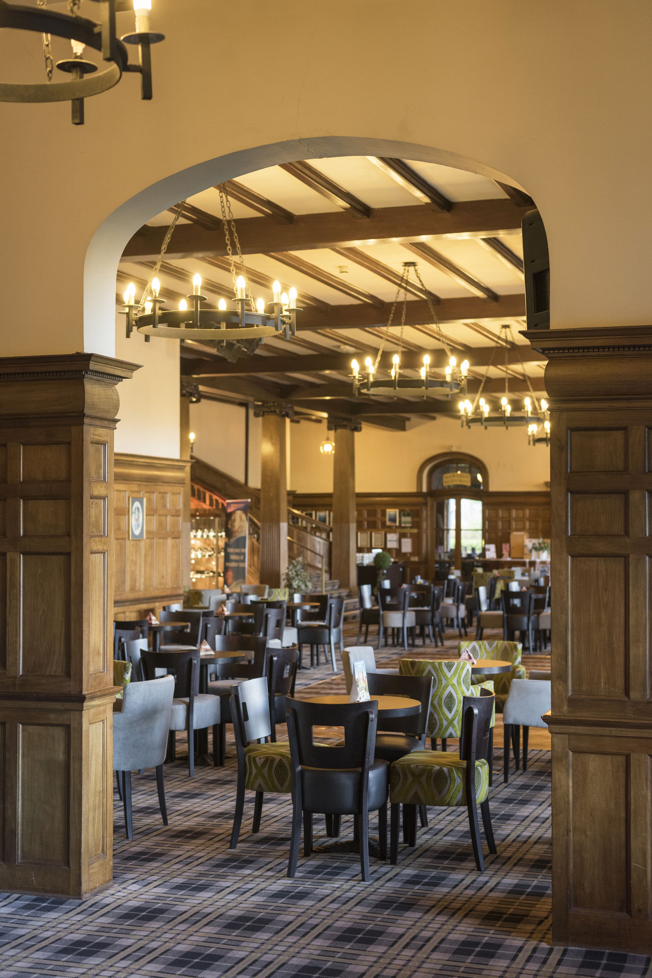 A spacious dining area with multiple tables and chairs, wooden paneling, and a high ceiling with chandeliers.