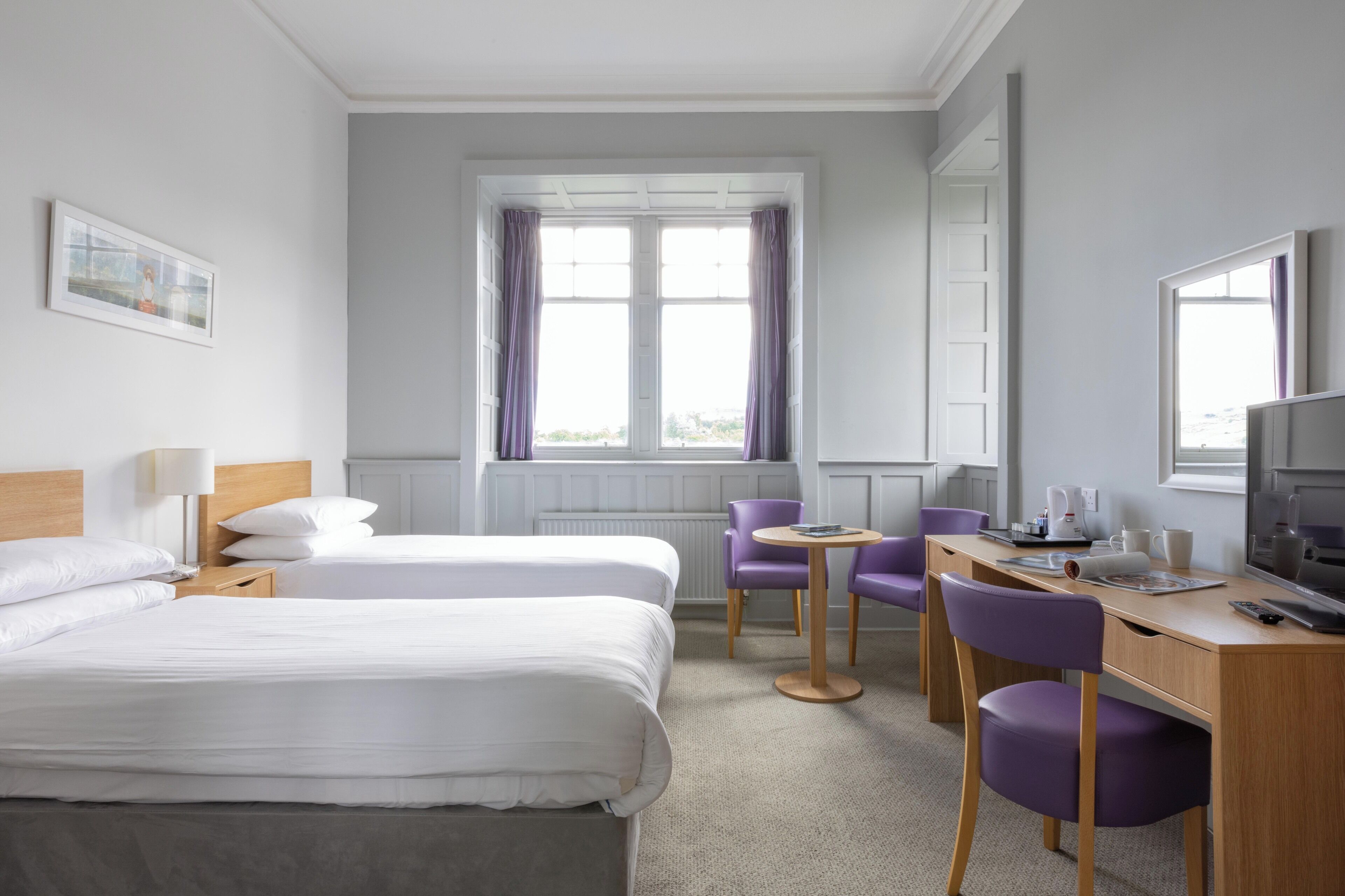 A hotel room with two beds, a desk with a computer, a chair, and a window with curtains.