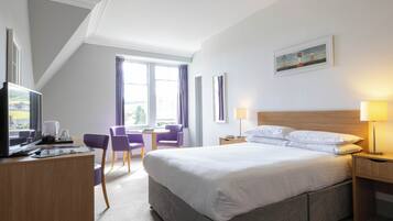 A hotel room with a large bed, a desk with a computer, a chair, and a window with curtains.