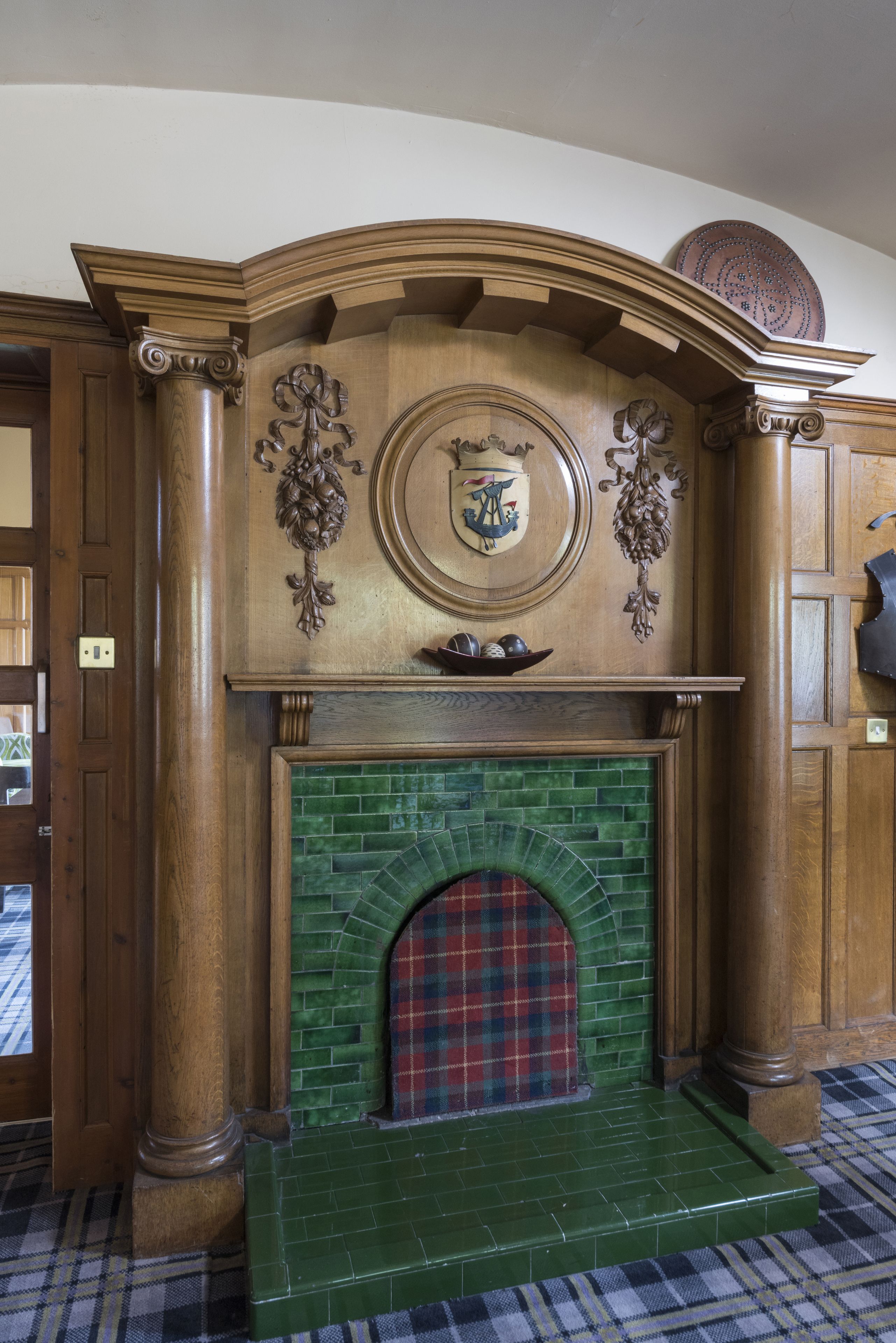 A fireplace with a green tiled surround and a plaid mantle.