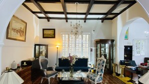 Amplia sala de estar con techo alto, candelabro, sofá, dos sillones, una mesa de centro y chimenea.