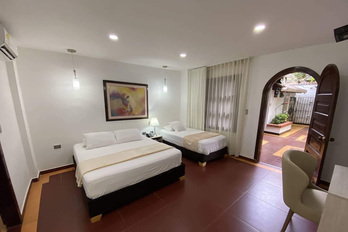 A hotel room with two beds, a painting on the wall, a desk with a lamp, and a view of the outside through a door.