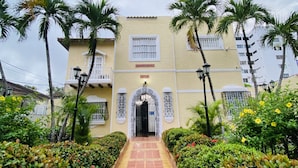 Un edificio con entrada central, rodeado de abundante vegetación y palmeras.