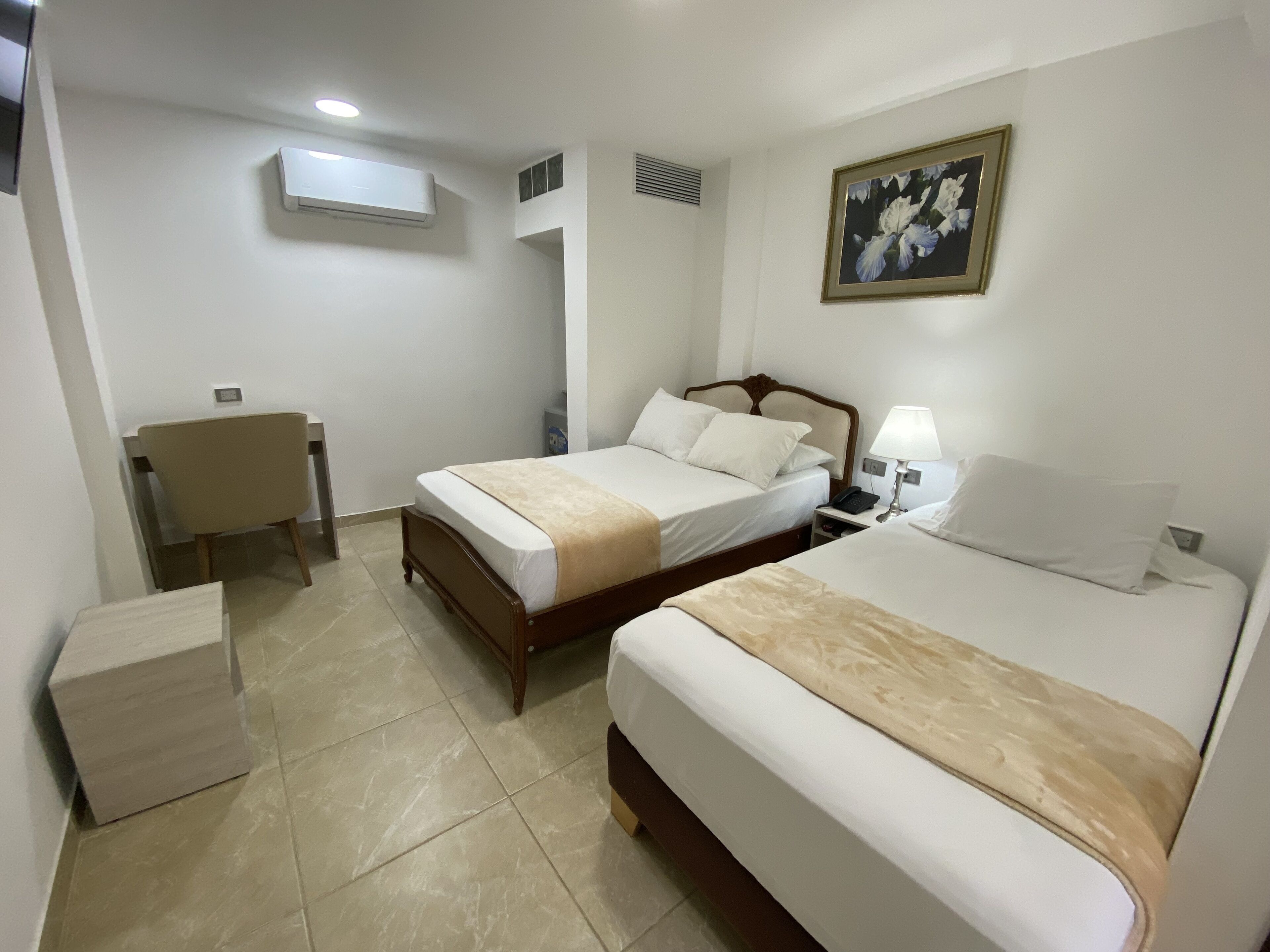 Camera d'albergo con due letti, una scrivania, una sedia, un comodino con una lampada e un quadro appeso al muro.
