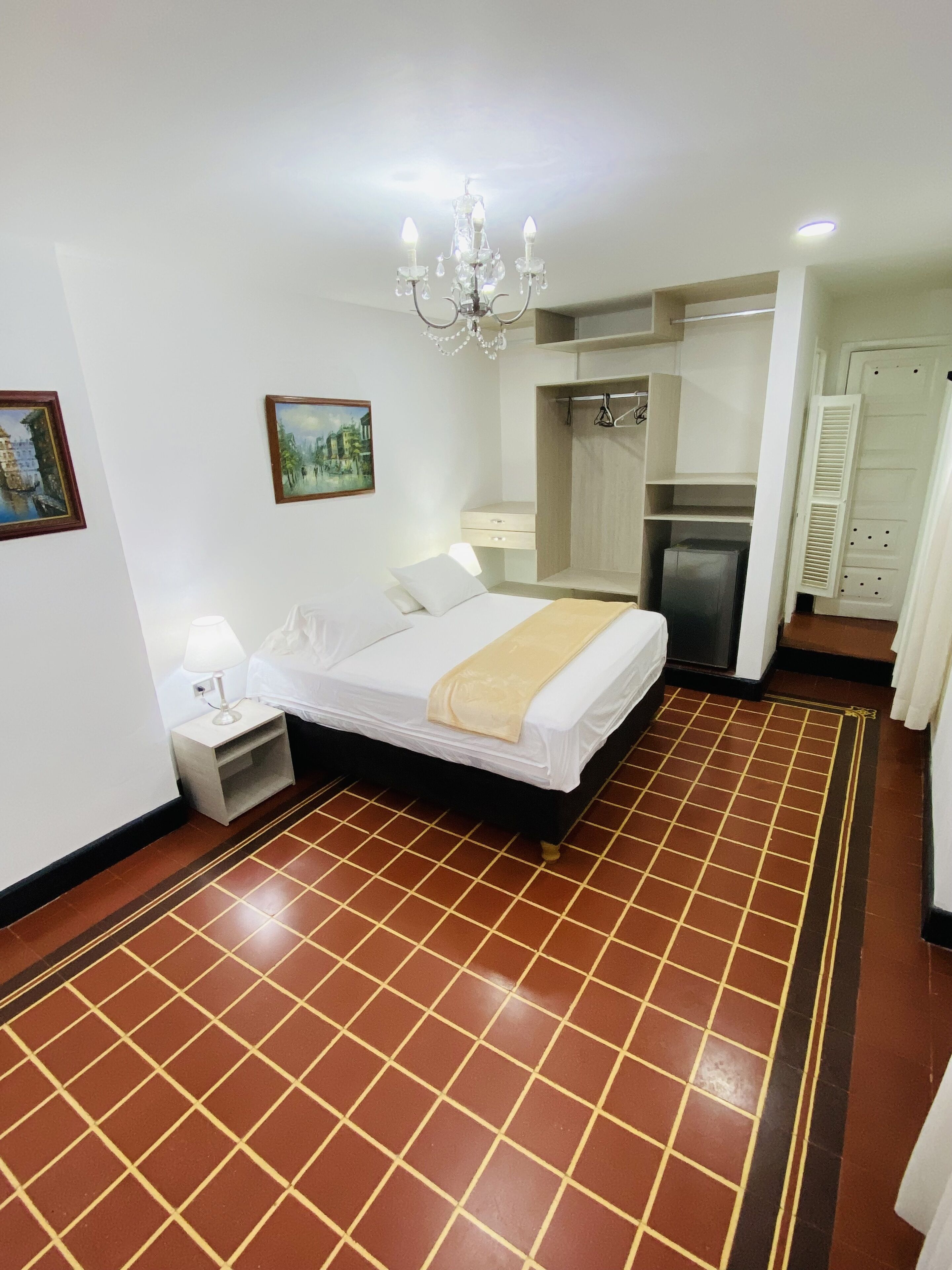 Una habitación de hotel con cama, mesita de noche, lámpara, candelabro y suelo de baldosas.
