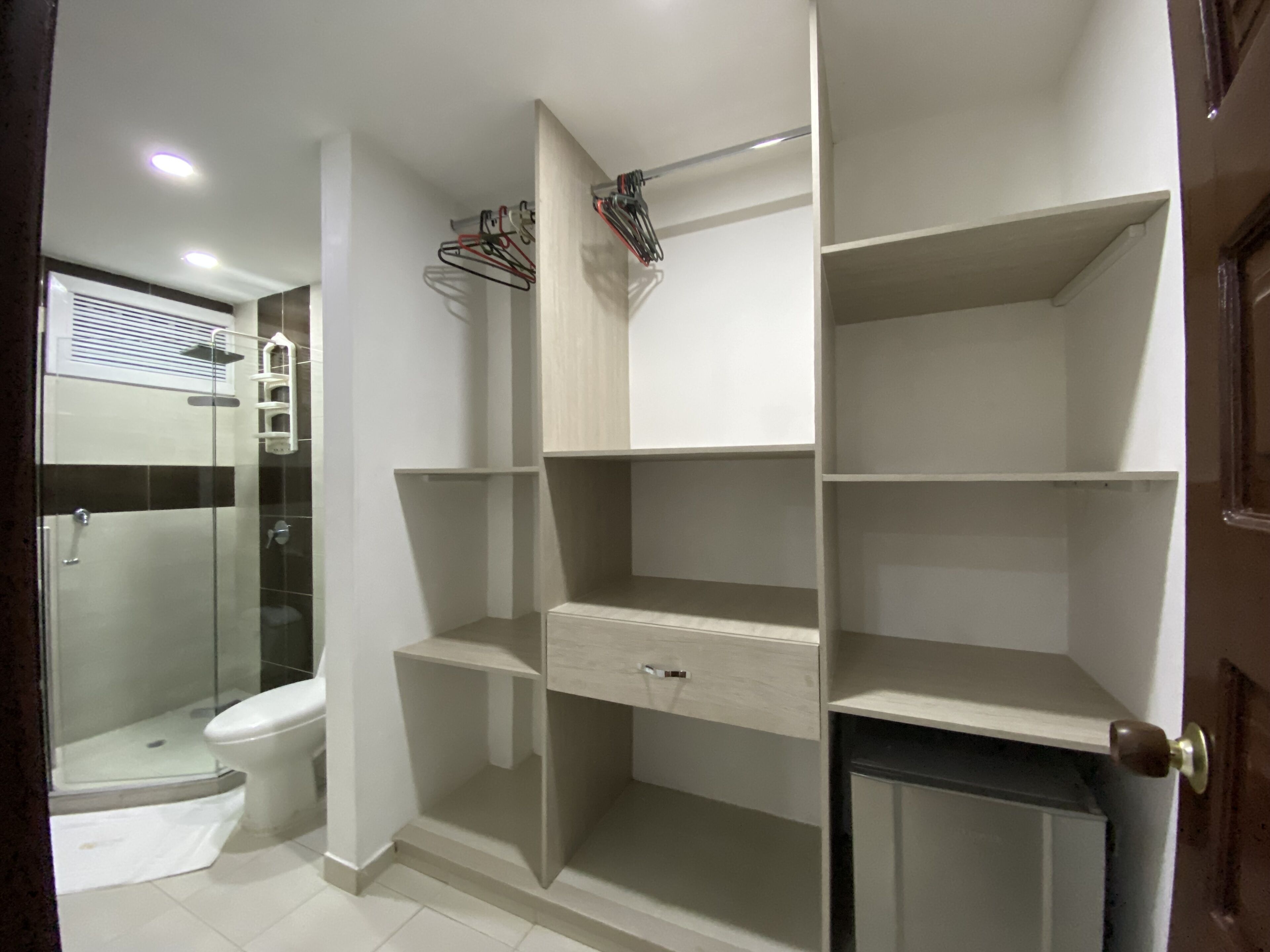 A bathroom with a glass shower enclosure, a toilet, and a built-in storage unit with shelves and drawers.