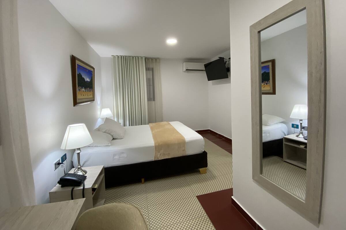 A hotel room with a bed, bedside table, lamp, and a large mirror.
