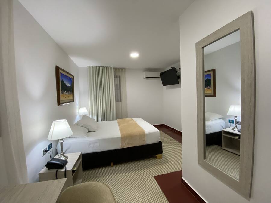 Een hotelkamer met een bed, nachtkastje, lamp en een grote spiegel.