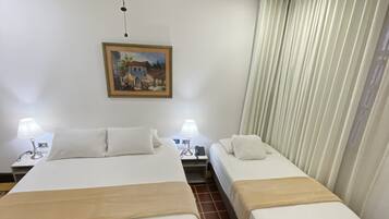 A hotel room with two beds, a ceiling fan, a painting, and a window with curtains.