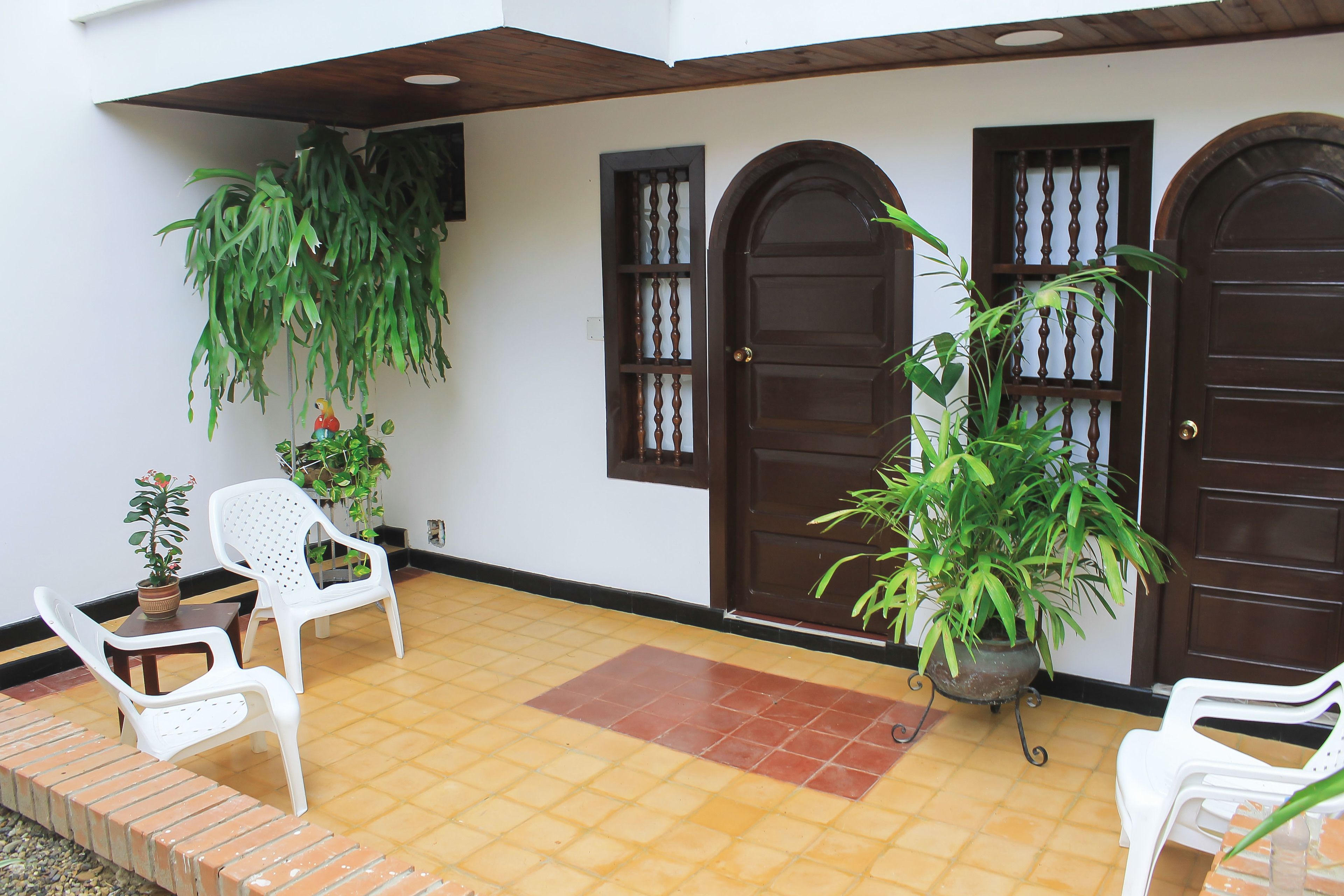 Un área de patio techada con piso de baldosas, sillas de plástico blancas y plantas en macetas.