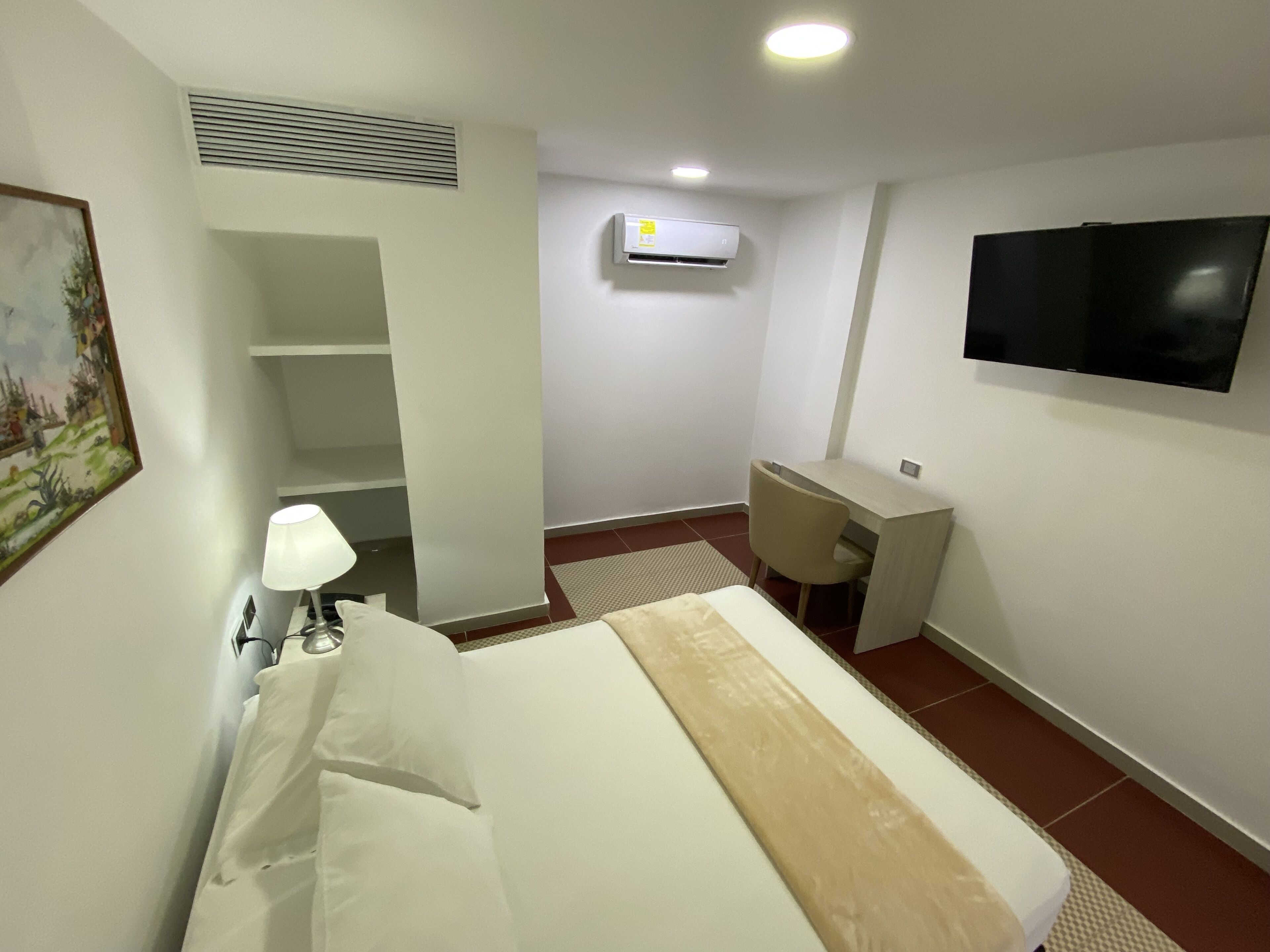 Une chambre d’hôtel avec un lit, un bureau, une chaise, une télévision, un climatiseur et un tableau au mur.