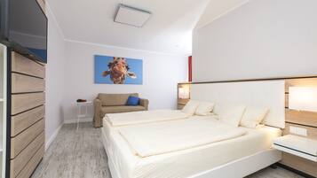 A modern hotel room with a large bed, a small table, a sofa, and a giraffe painting on the wall.