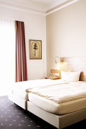 Habitación de hotel con cama, mesita de noche, lámpara, un cuadro en la pared y ventana con cortinas.