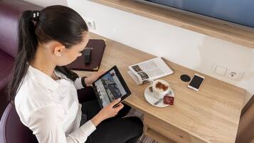 A person sitting at a wooden table with a tablet, a smartphone, a cup of coffee, and a notebook.
