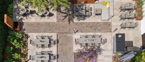 Un patio al aire libre con varios arreglos de asientos, incluyendo mesas y sillas, rodeado de follaje y plantas.